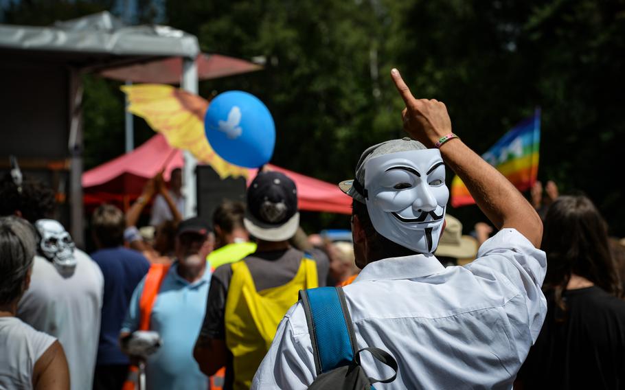 An audience member wearing a Guy Fawkes mask cheers stage perfomers during an anti-war protest in Ramstein-Miesenbach, June 25, 2022.