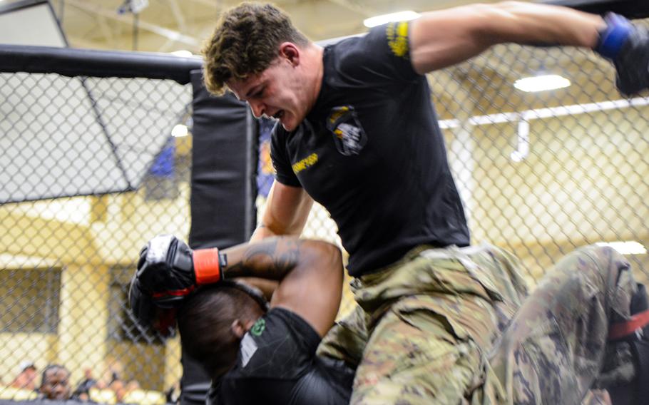 Two fighters in a cage, one on the ground, shielding his face with his arms as the other is on top of him.