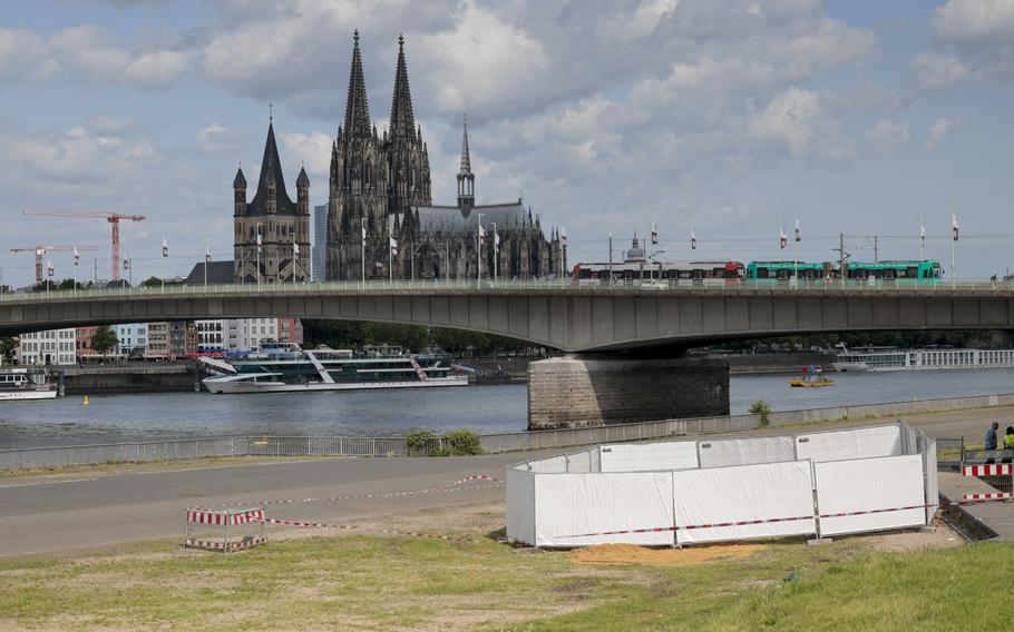 Cologne’s historic buildings seen in the background as a series of screens enclose an area by a river in the foreground.