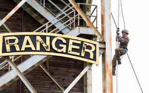 A soldier climbs a rope, next to a giant sign that says Ranger.