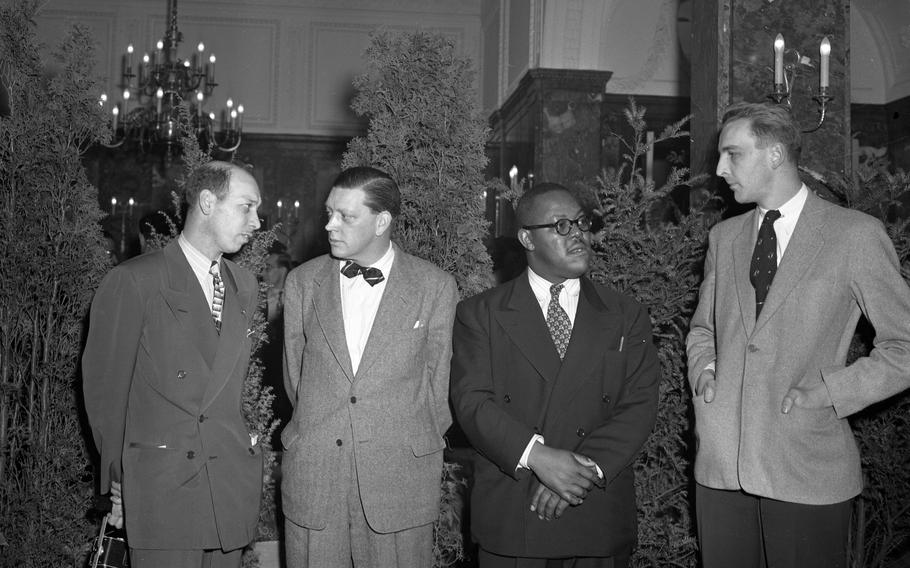 A black and white photo of four men in suits talking to one another.