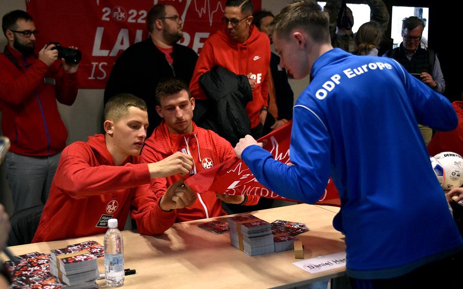 Midfielder Aaron Basenach, left, and forward Daniel Hanslik, right, of 1. FC Kaiserslautern, sign a fan's flag on March 23, 2023, at Ramstein Air Base, Germany.