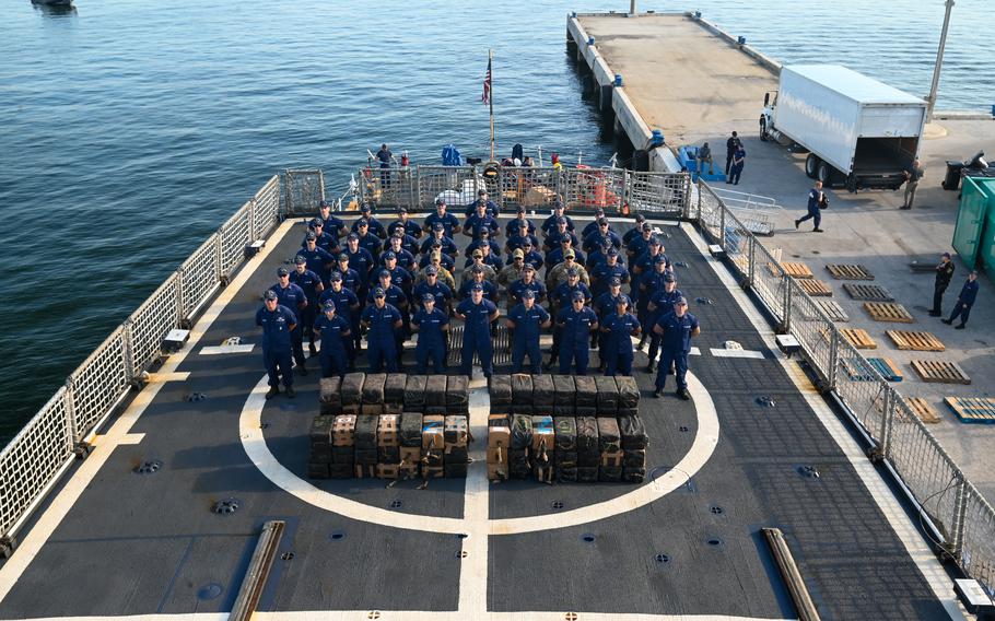 A Coast Guard cutter crew stands in formation behind stacks of seized contraband.