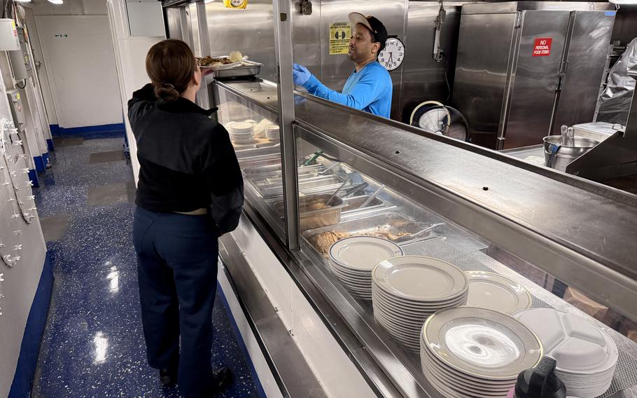 A food service worker hands a plate of food to a sailor.