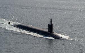 The top of a military submarine is seen above the water line as it transits open sea.