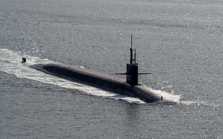 The top of a military submarine is seen above the water line as it transits open sea.