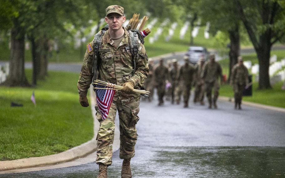 A soldier walks down a road with flags in hand.