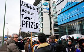 A demonstrator holds a placard reading "Scammer, thief, killer, Pfizer" during a protest against the vaccine pass and vaccinations to protect against COVID-19 in front of the Pfizer headquarters, in Paris, on Jan. 29, 2022.