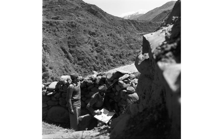 Guards look out over a sentry position in a hilly area.
