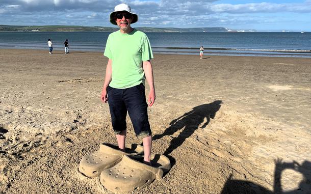 A man stands in a pair of Crocs made of sand. 