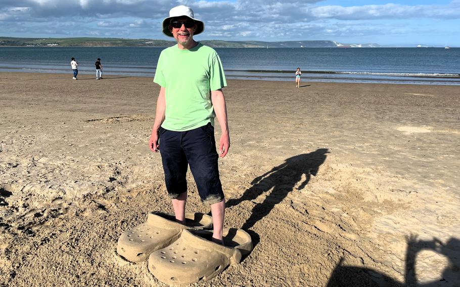 A man stands in a pair of Crocs made of sand. 