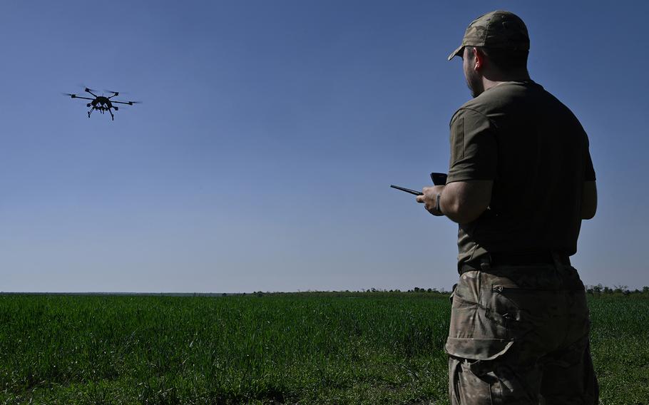 A service man seen from behind, operating a drone on a sunny day.