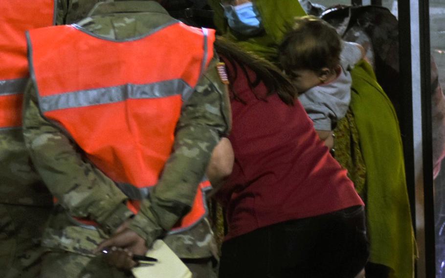 A woman holding a small child steps off the bus at Ramstein Air Base, Germany, on Friday, Aug. 20, 2021, after arriving on a U.S. military flight from Al Udeid Air Base, Qatar. 