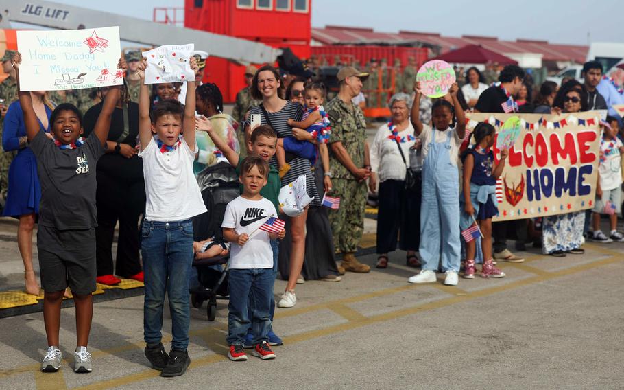 Families of sailors hold signs, one says Welcome Home.