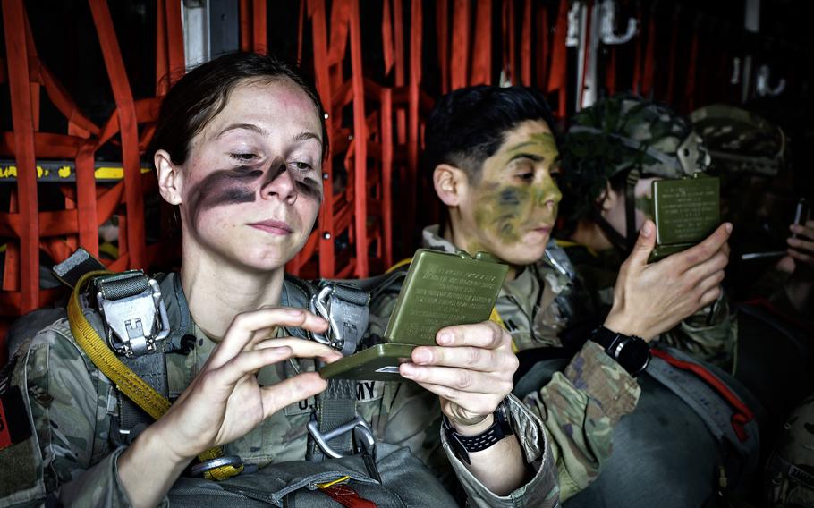 Two U.S. Army paratroopers apply camouflage to their faces.