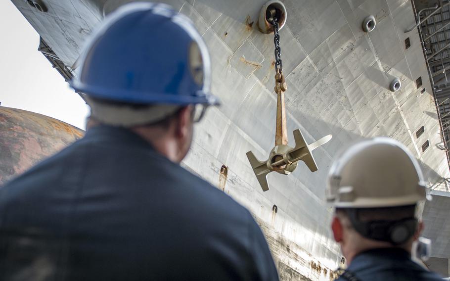 Sailors watch as the aircraft carrier USS George H.W. Bush's portside anchor is lowered into a dry dock for maintenance at Norfolk Naval Shipyard, Va., March 15, 2019.