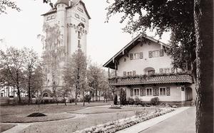 A black and white photo shows a tall brick building next to a nice home with a manicured lawn. 
