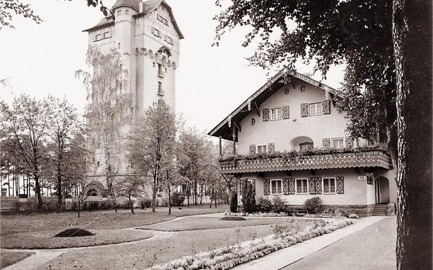 A black and white photo shows a tall brick building next to a nice home with a manicured lawn. 