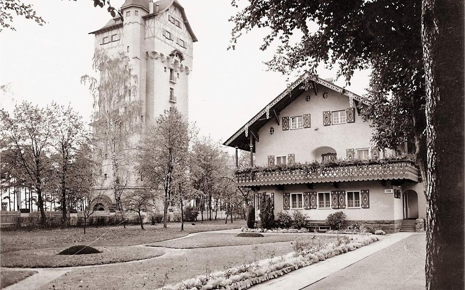 A black and white photo shows a tall brick building next to a nice home with a manicured lawn. 