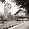 A black and white photo shows a tall brick building next to a nice home with a manicured lawn. 
