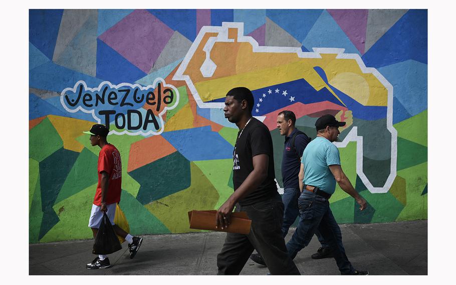 People walk by a mural in the 23 de Enero neighborhood in Caracas on Nov. 28, 2023, campaigning for a referendum to ask Venezuelans to consider annexing the Guyana-administered region of Essequibo. 