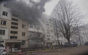 Firefighters on the ground aim hoses into the top floors of a burning housing complex.