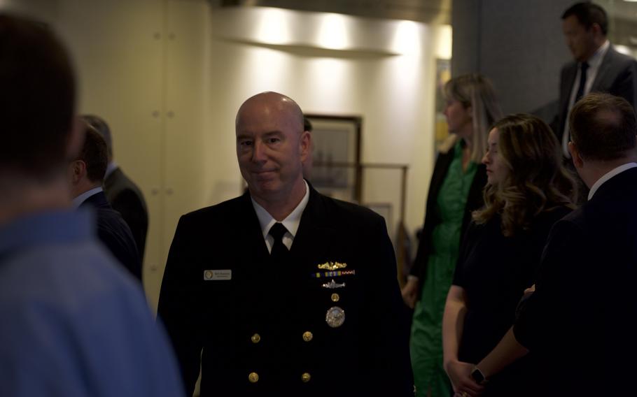A man in a Naval uniform with several pins and medals looks at the camera.