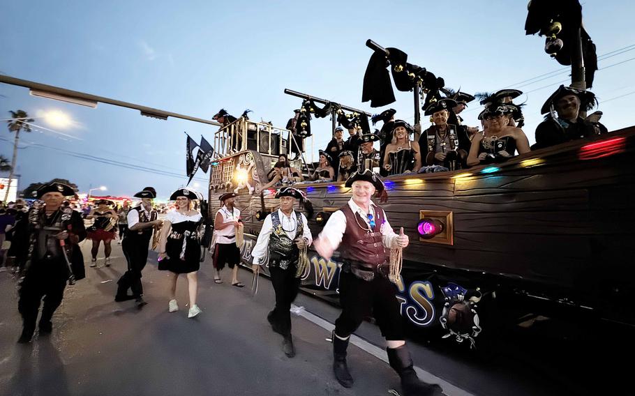 People dressed as pirates walk next to a replica pirate boat.