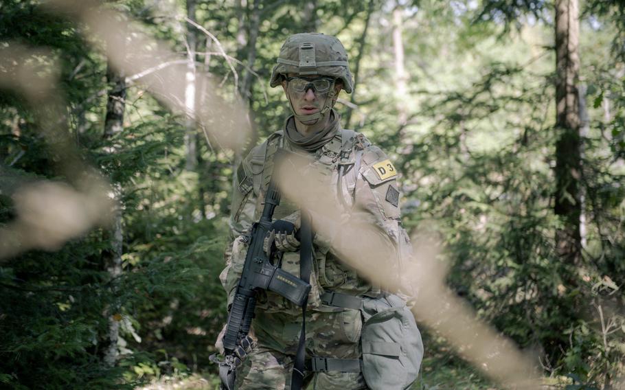 A soldier on patrol, seen through tree branches and leaves.