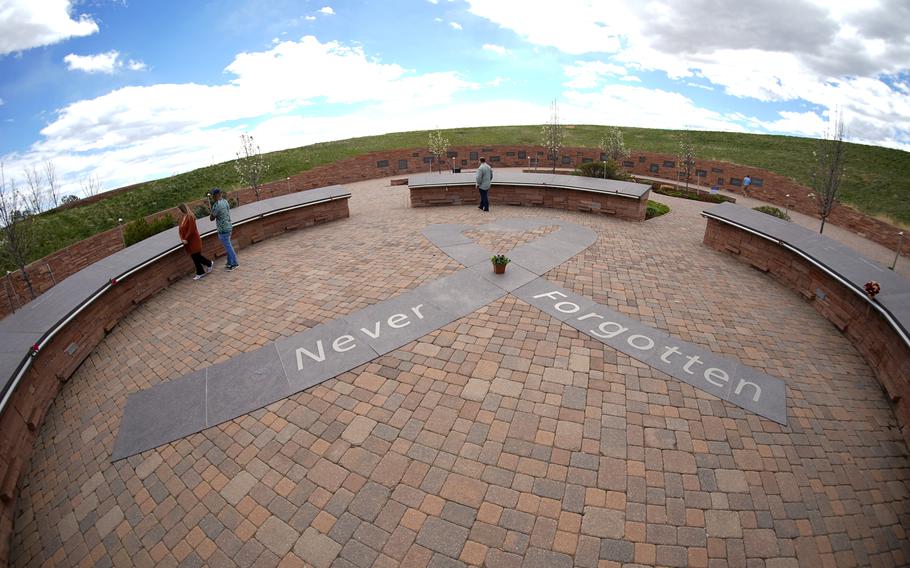 In this photo taken with a fisheye lens, people visit the Columbine Memorial, April 17, 2024, in Littleton, Colo. The 12 students and a teacher killed in the Columbine High School shooting will be remembered Friday, April 19, 2024, in a vigil on the eve of the 25th anniversary of the tragedy.