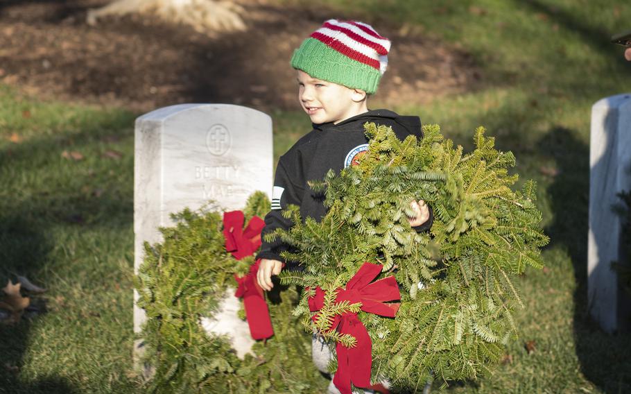 Nick Laverick carries a wreath before it is placed on a tombstone at Arlington National Cemetery on Saturday, Dec. 17, 2022.