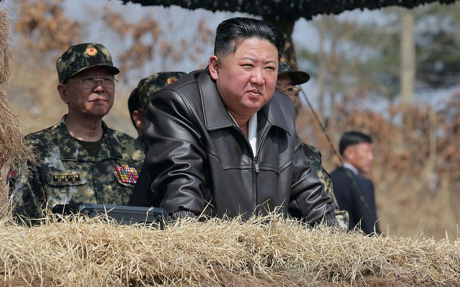 Kim Jong Un, wearing a black leather jacket, stands in a military bunker with officials in camouflage uniforms behind him.