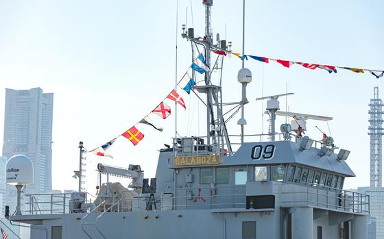 The bridge of a U.S. military vessel is shown with a ribbon of foreign flags flying above it.