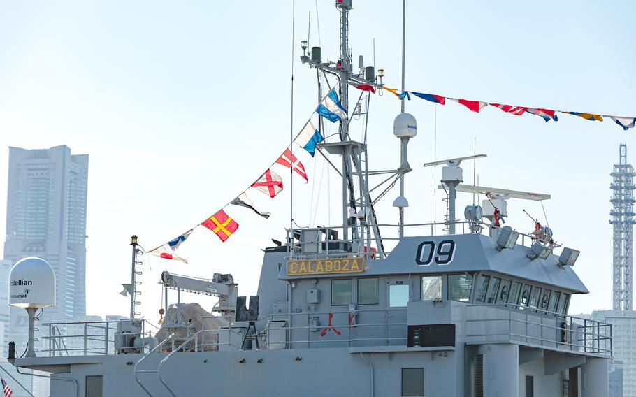 The bridge of a U.S. military vessel is shown with a ribbon of foreign flags flying above it.