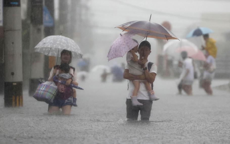 People wade through a road flooded by heavy rain in Kurume, Fukuoka prefecture, western Japan, Saturday, Aug. 14, 2021. Torrential rain continued to trigger floods Saturday in wide areas of southwestern Japan, damaging homes and disrupting transportation. 