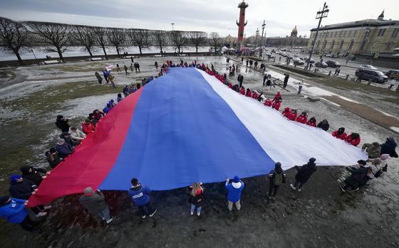 Young people unfurl a giant Russian flag during an action to mark the ninth anniversary of the Crimea annexation from Ukraine in St. Petersburg, Russia, Saturday, March 18, 2023. (AP Photo/Dmitri Lovetsky)