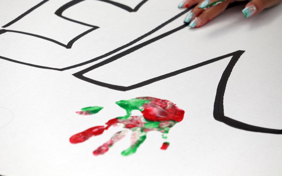 A close-up view of a green and red handprint on a white poster board.