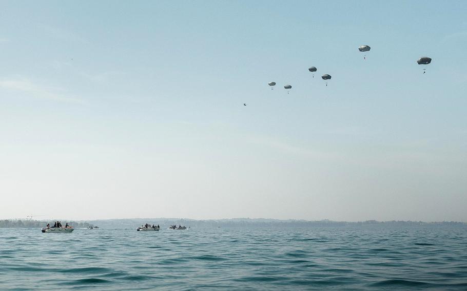 Several paratroopers are seen descending over a body of water from a distance.