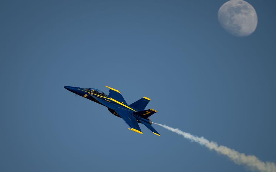 A jet flies fast, with smoke trailing and the moon in the background.