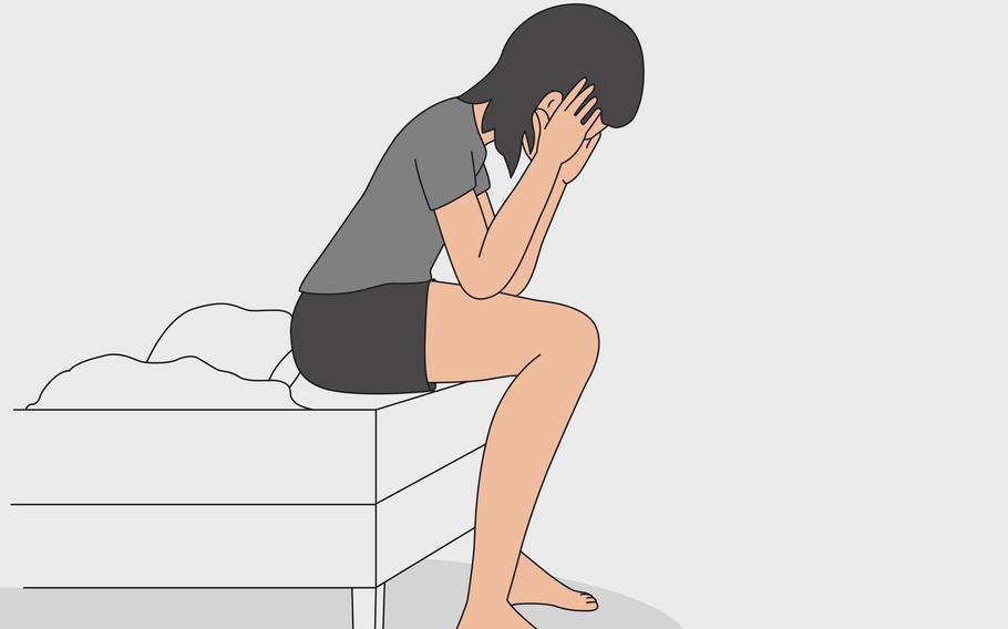 A woman sits on the edge of the bed and holds onto her head