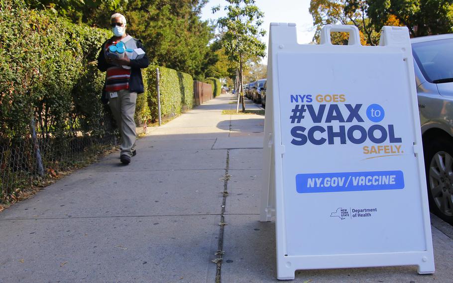 A man carrying cleaning supplies prepares to walk past a sign announcing a #VAXTOSCHOOL pop-up site at Life of Hope Center on Thursday, Oct. 21, 2021 in New York.