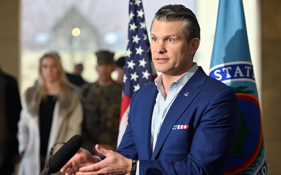 Pete Hegseth holds his hands out while talking, with a U.S. flag in the background
