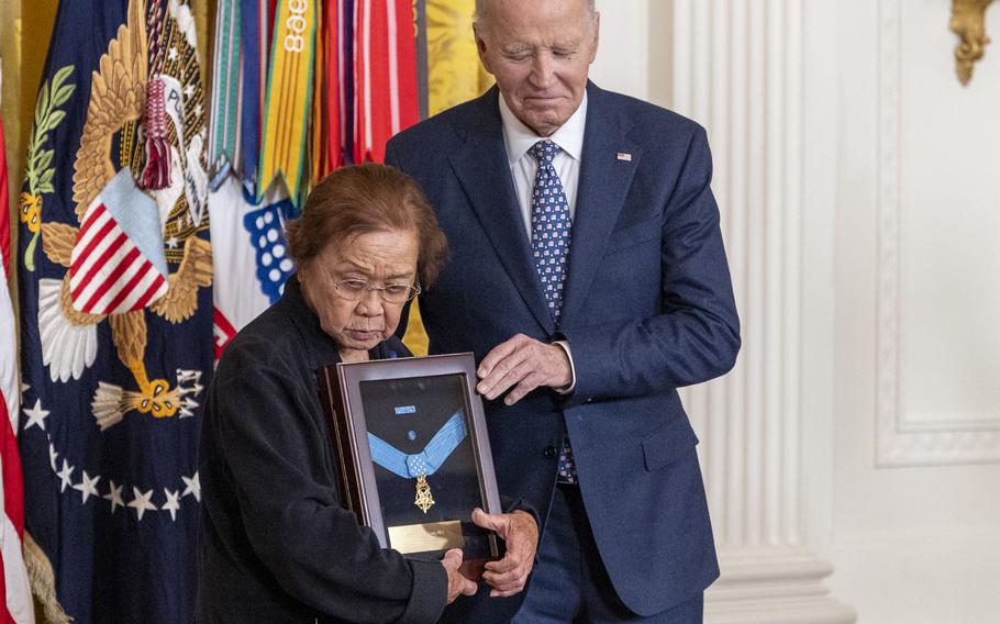 An elderly woman holds a framed Medal of Honor awarded posthumously to her brother while standing next to Joe Biden.