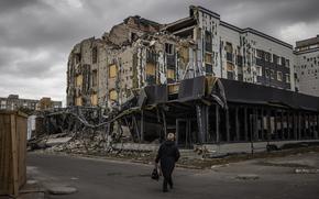A person walks by a partially destroyed building on a cloudy day.