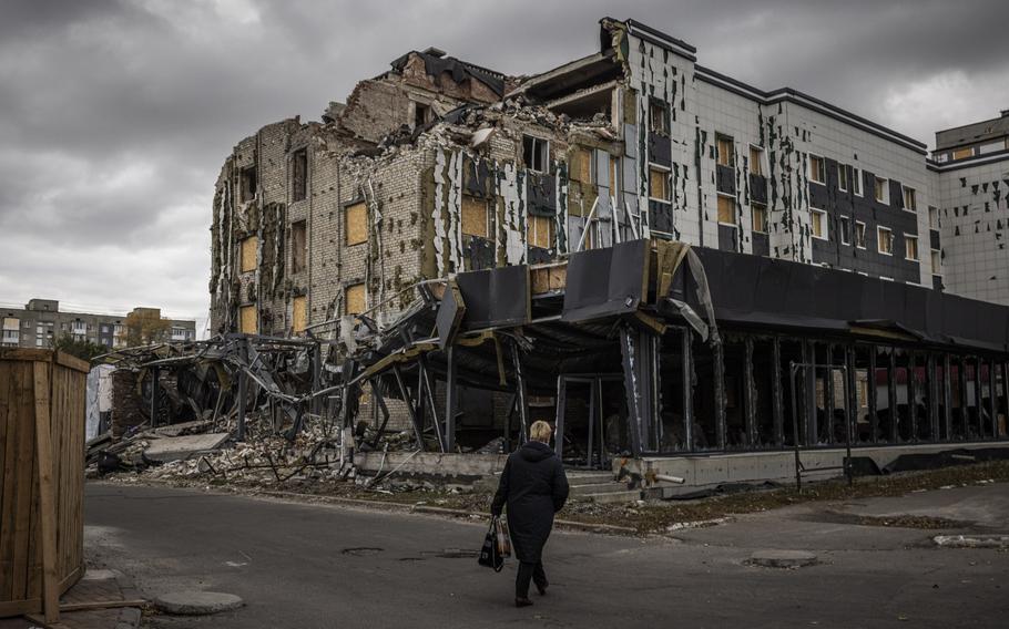 A person walks by a partially destroyed building on a cloudy day.