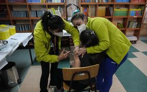 Healthcare workers give a child a booster shot of the pediatric Pfizer COVID-19 vaccine at Paul Harris School in Santiago, Chile, Friday, May 13, 2022. 