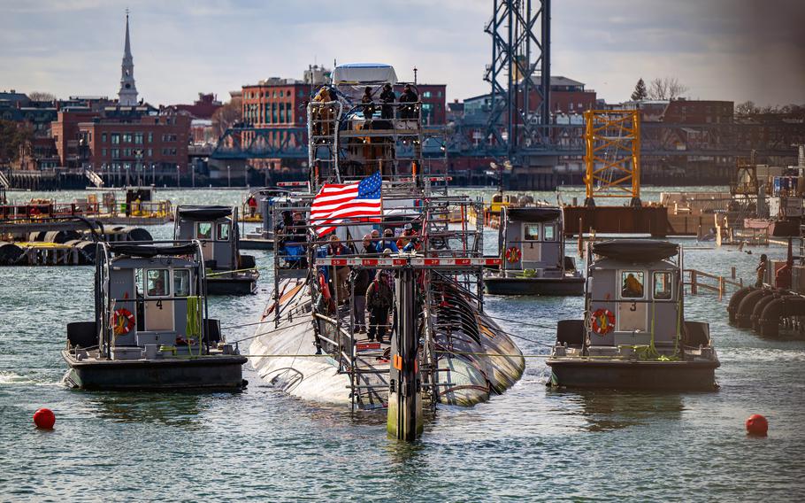 A submarine flying an American flag moves into dry dock flanked by two small boats.