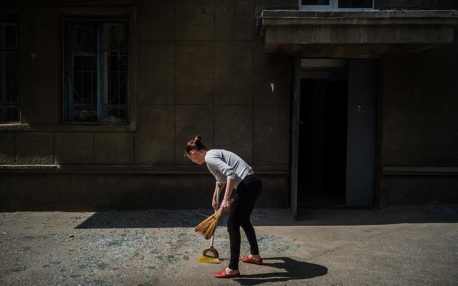 Tatiana Andrienko sweeps glass from the sidewalk in front of her apartment building on May 3, 2022, after a Russian rocket hit a nearby area of Kharkiv. 
