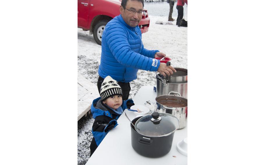 Mads Ole Kristiansen, an Inuit from Qaanaaq, with his son Suikkaq, 2, gets another helping of seal stew. A group of Inuit locals demonstrated local culture and provided food in front of a small but appreciative and apprehensive crowd watching from the Thule Air Base main pier.