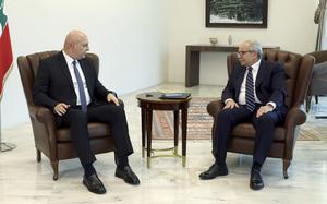 Two men in suits sit in sofa chairs and look at one another.